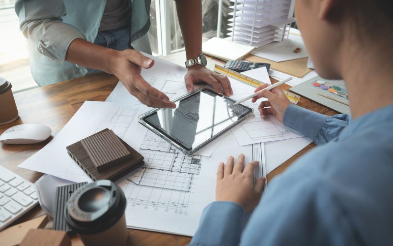 Architects and interior designers women discussing to concept of building design. Estimation for construction project with tablet technology, Drawing, Material and Model. Selective focus center image
